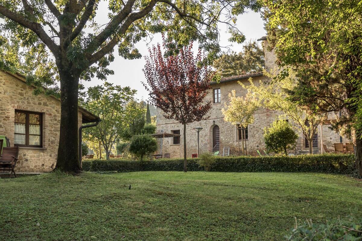 Un bâtiment en pierre, avec un grand arbre au premier plan, une pelouse bien entretenue et un mur de pierre en arrière-plan.
