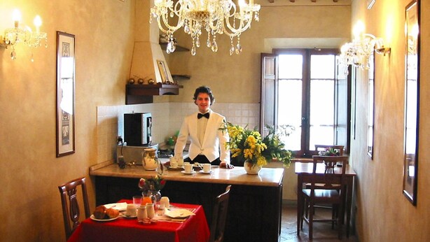 Une salle à manger agrémentée d’un lustre, un chef cuisinier vêtu d’une veste blanche et une nappe rouge.