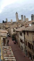 Una stretta via fiancheggiata da edifici storici in pietra, con un'auto rossa parcheggiata sul lato e una torre sullo sfondo.