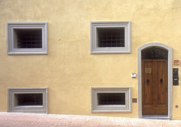 Fachada de edificio con tres ventanas cuadradas y una puerta de madera con un letrero encima.
