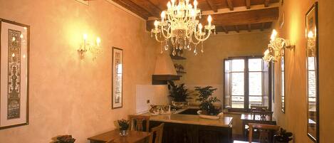Un comedor con mesas y sillas de madera, una araña y cuadros en las paredes.