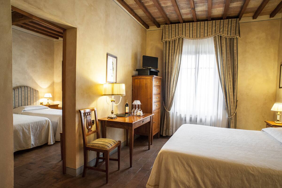 Quarto de hotel com duas camas, uma escrivaninha com cadeira, cómoda e janela com cortinas.