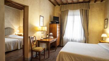 Habitación de hotel con dos camas, un escritorio con silla, cómoda y ventana con cortinas.