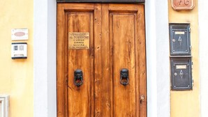 Une porte à deux battants en bois, ornée d’une plaque, d’une arche décorative en métal et d’une boîte aux lettres située à droite.