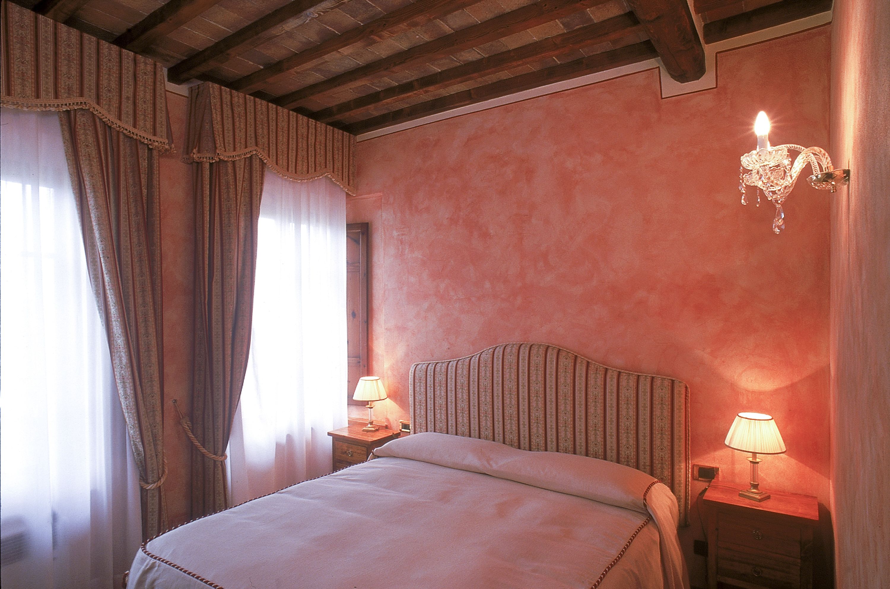 A bedroom with a bed, two bedside tables with lamps, a chandelier, and curtains.