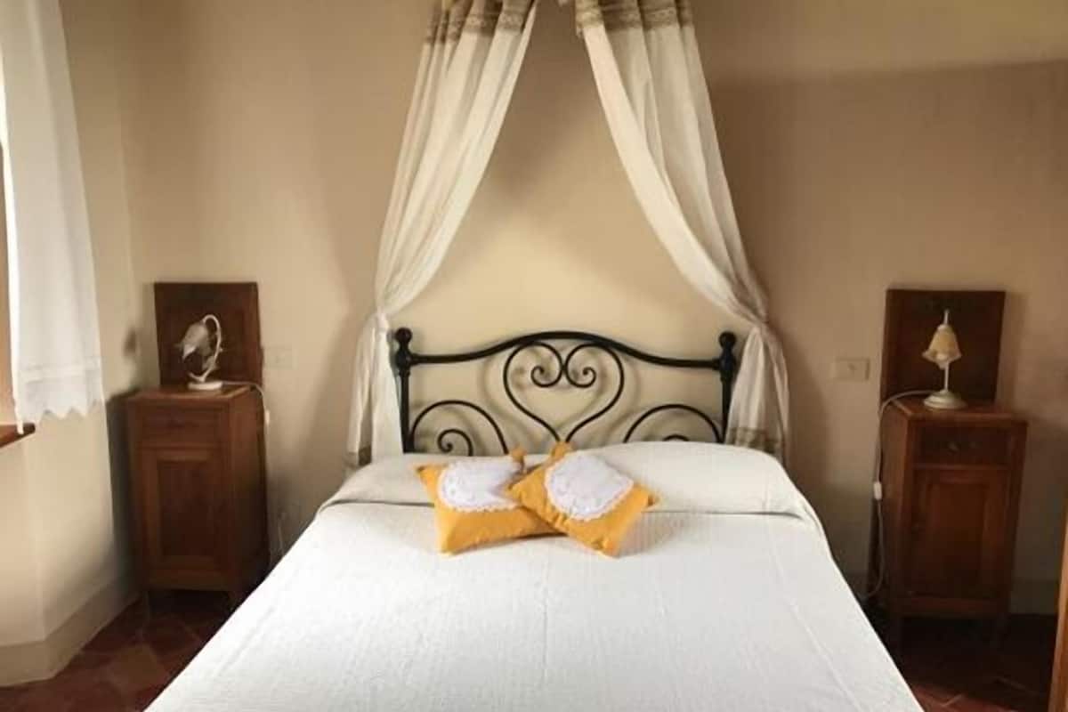 Un dormitorio con una cama con dosel, ropa de cama blanca y dos mesitas de noche con lámparas.