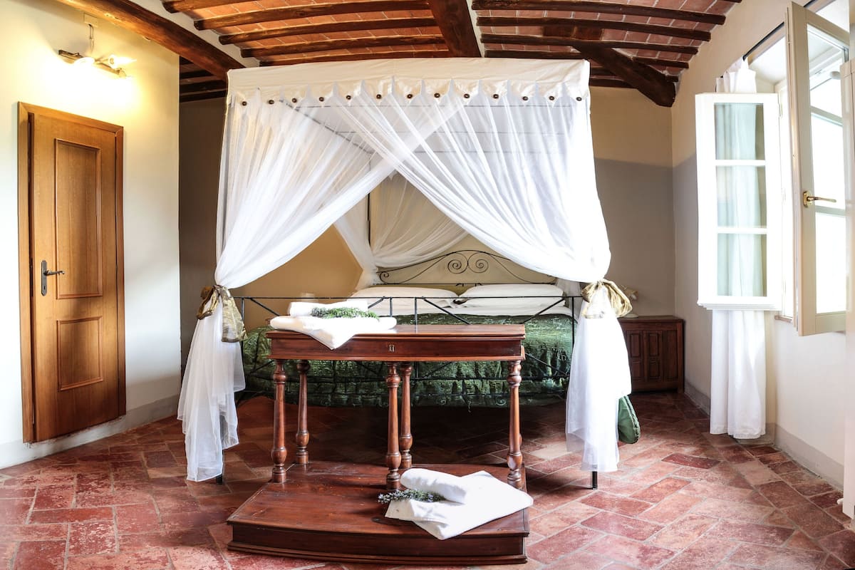 Una habitación con una cama con dosel, una mesa de madera cubierta con tela blanca y un banco de madera.