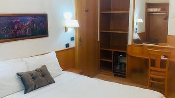 A hotel room with a large bed, a desk, a wardrobe, and a chandelier.