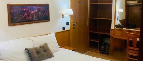 A hotel room with a large bed, a wooden wardrobe, a desk with a chair, a mirror, and a chandelier.