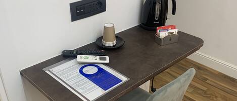 Un espacio de trabajo moderno y pequeño, con escritorio, silla, cafetera y control remoto.