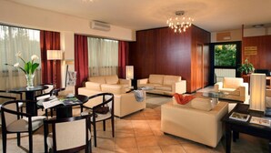A modern living room with a sofa set, a coffee table, and a dining area with chairs and a table. - Cassia Hotel (Rome)