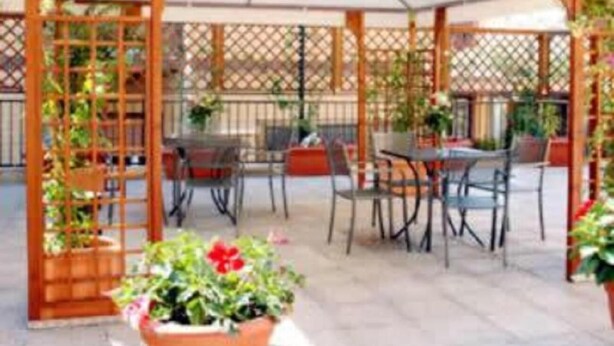 An outdoor patio area with a covered seating area, wooden lattice structure, and potted plants. - Cassia Hotel (Rome)