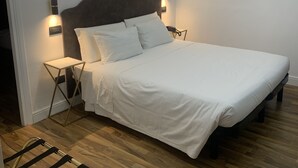 A neatly made bed with white linens, a wooden floor, a wall-mounted air conditioner, and a decorative gold leaf mirror. - Cassia Hotel (Rome)