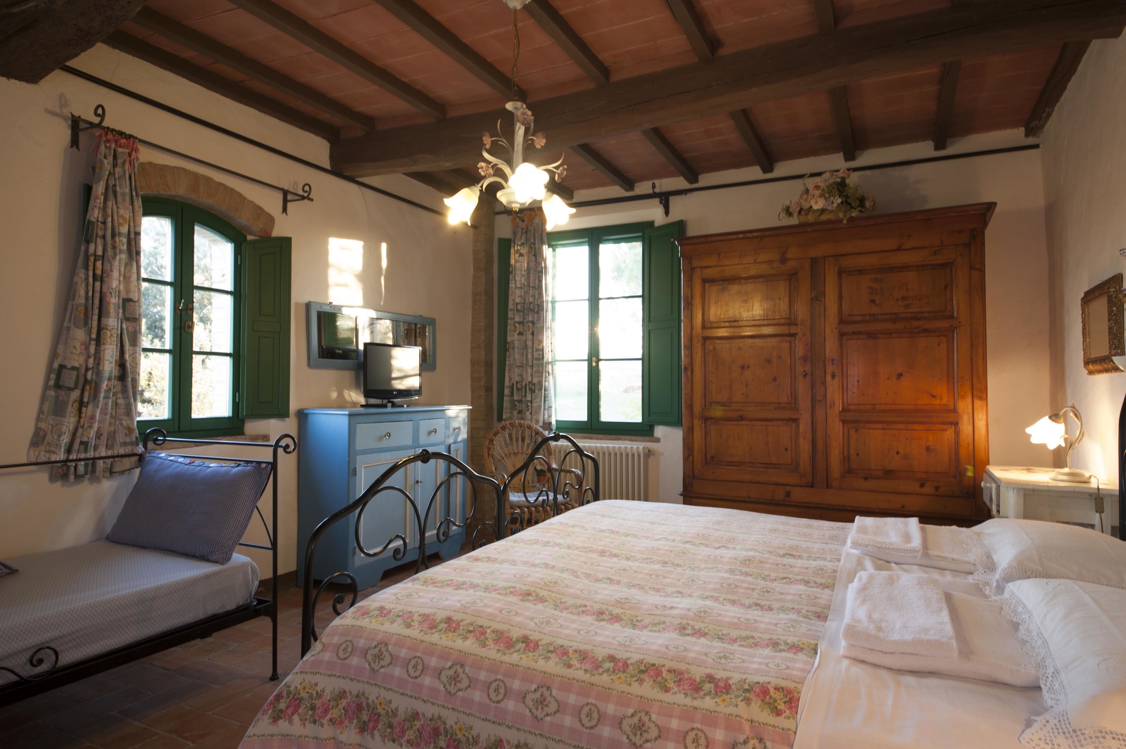 Une chambre à coucher avec un lit, un petit bureau, une chaise, une commode et une fenêtre avec des rideaux.