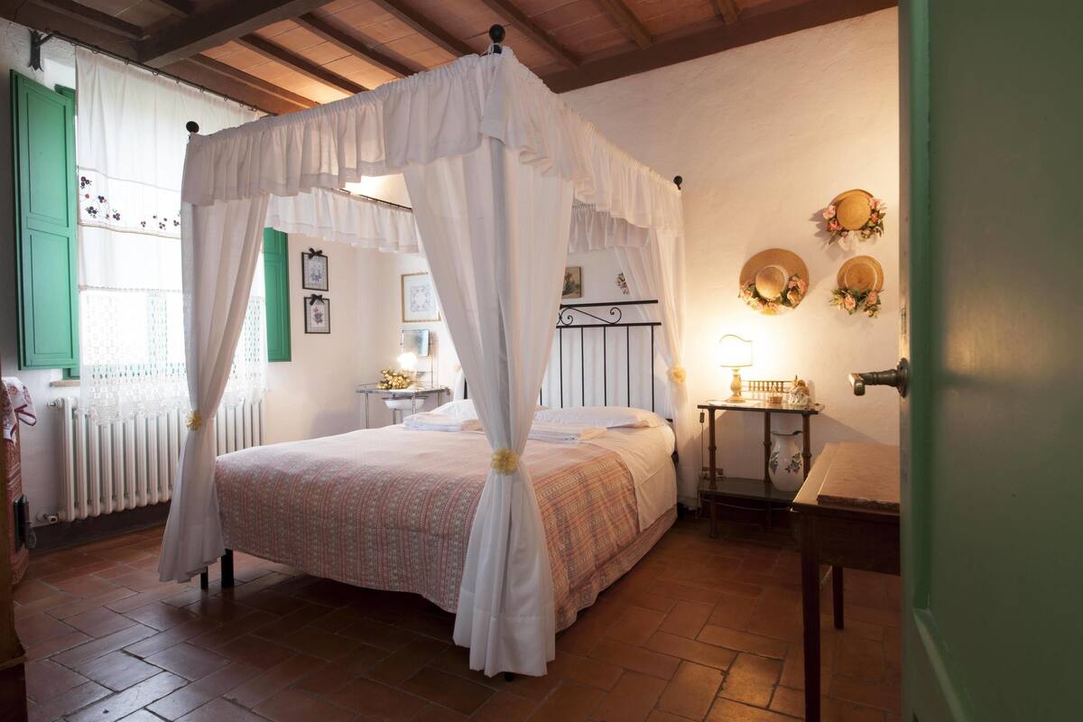 Un dormitorio con una cama con dosel, una mesita de noche con lámpara y una puerta verde.