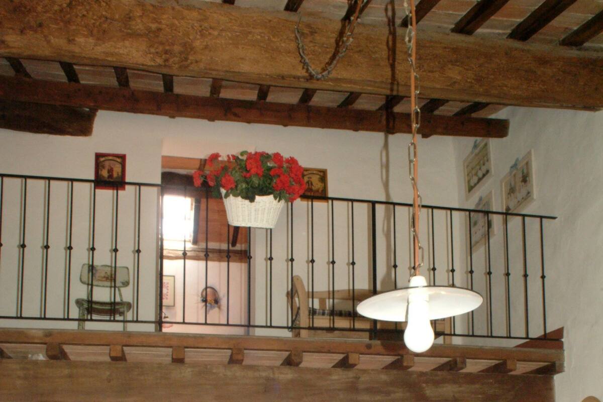 Un dormitorio con cama de madera, una mesita de noche pequeña, una cesta de flores colgante y un balcón con barandilla.