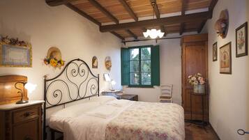 Une chambre à coucher avec un lit, une tête de lit en bois, une table de chevet avec une lampe, une commode, une fenêtre avec des volets verts et une porte en bois.