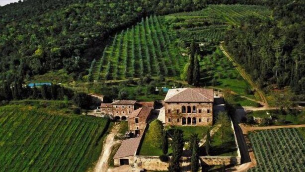 Vue aérienne d’un domaine rural avec des champs en terrasses, un grand bâtiment en pierre doté d’arcades et une végétation luxuriante environnante.