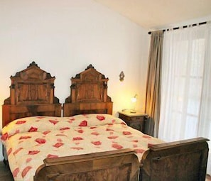 A room with a wooden bed, a bedside table with a lamp, and a window with curtains.