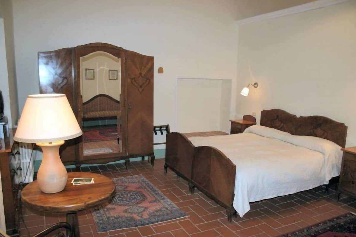 Une chambre à coucher comprenant un lit, une table de chevet en bois, une lampe de chevet, un miroir et une petite table avec une lampe.