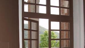 Une paire de portes doubles donne sur un balcon offrant une vue sur la verdure et les collines.