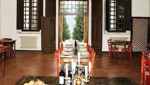Une salle à manger avec un lustre, une table dressée pour le repas et une vue sur l’extérieur par une porte ouverte.