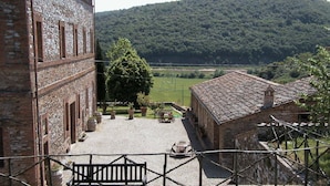 Une cour avec un banc, un bâtiment à la façade en pierre et une vue sur une colline boisée.