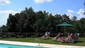 Une piscine entourée d’une clôture en bois et d’arbres, avec des chaises longues et des parasols à proximité.
