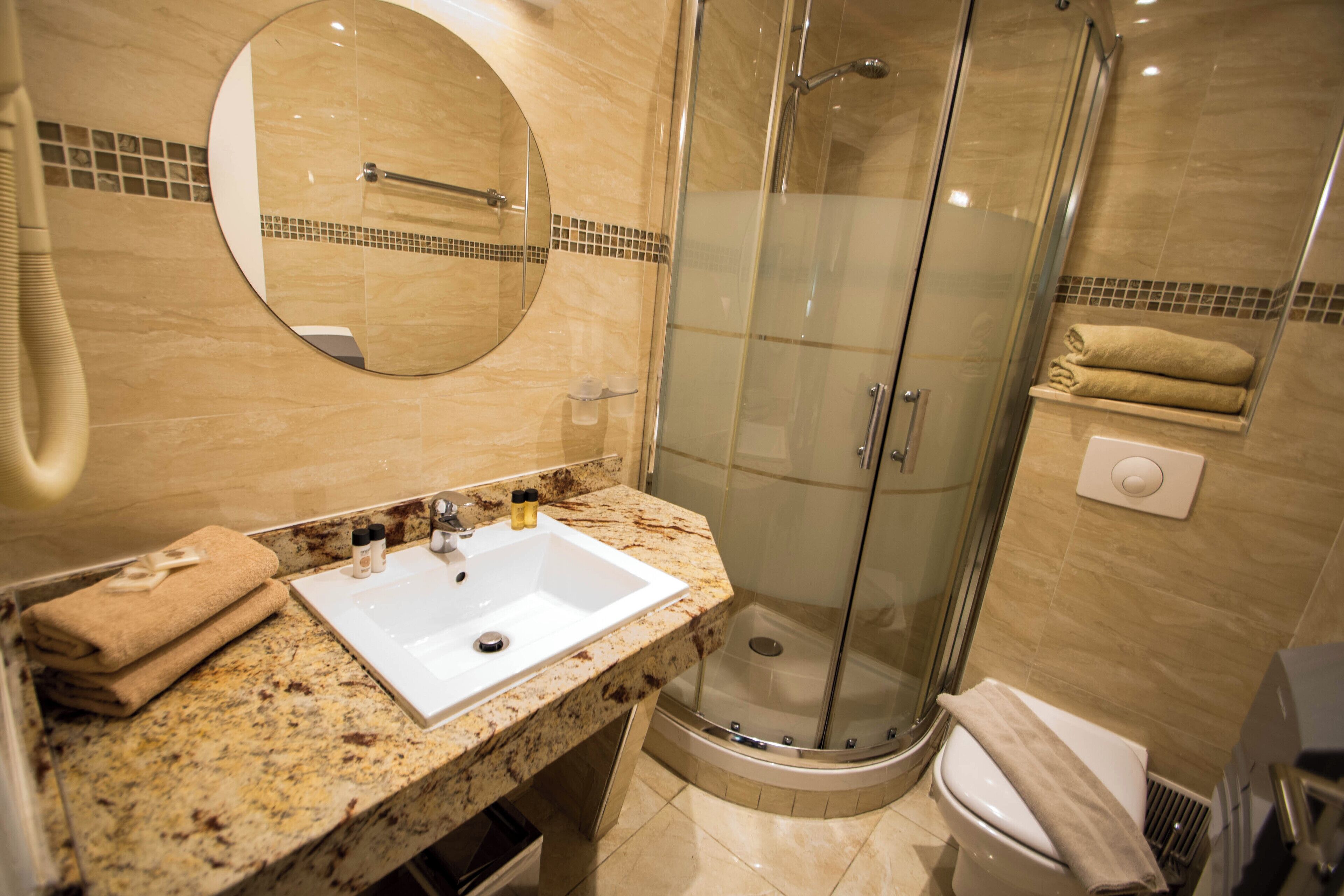 A bathroom with a sink, mirror, shower, and toilet.