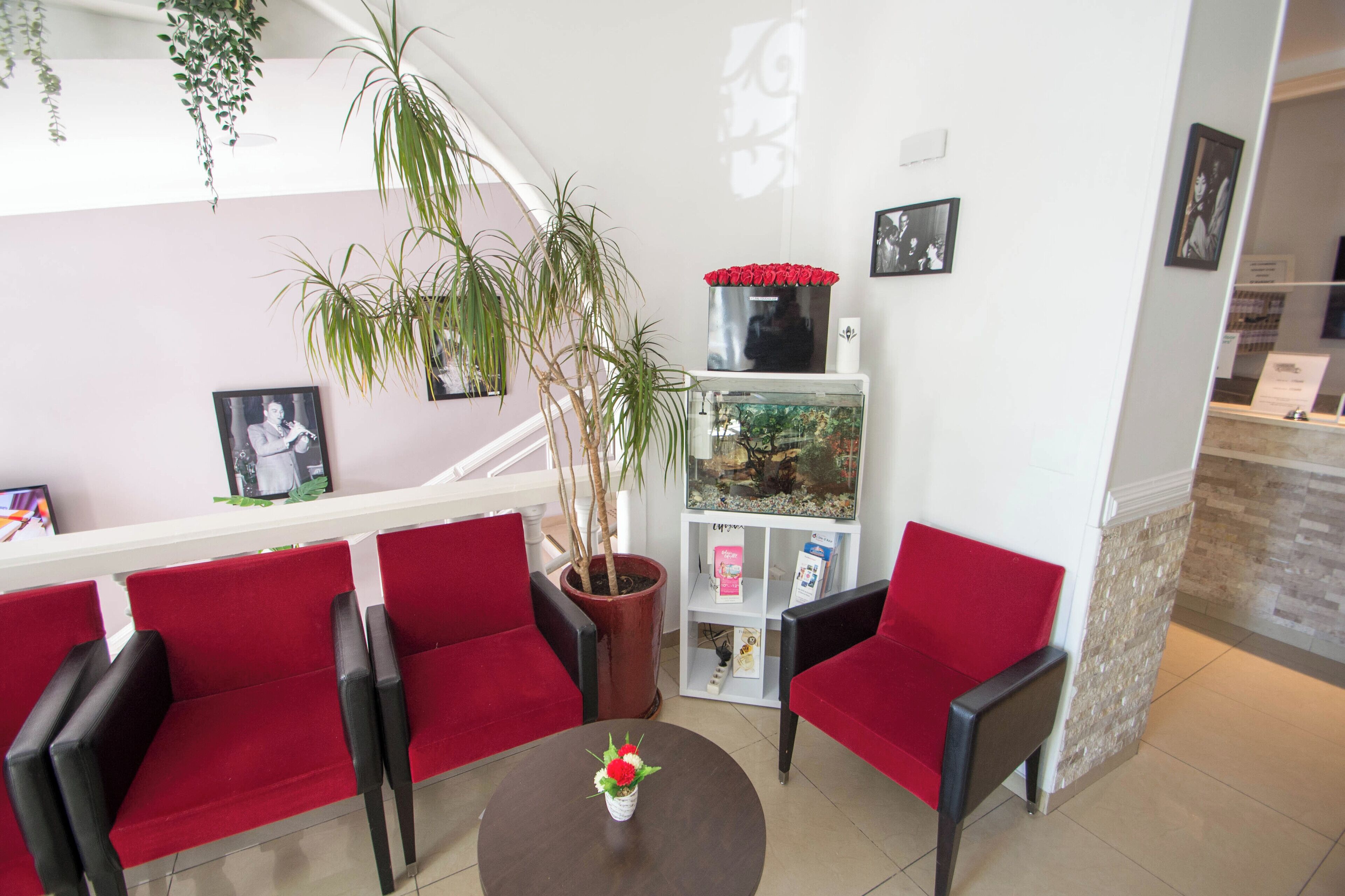 A reception area with red chairs, a potted plant, a fish tank, and framed pictures on the wall.