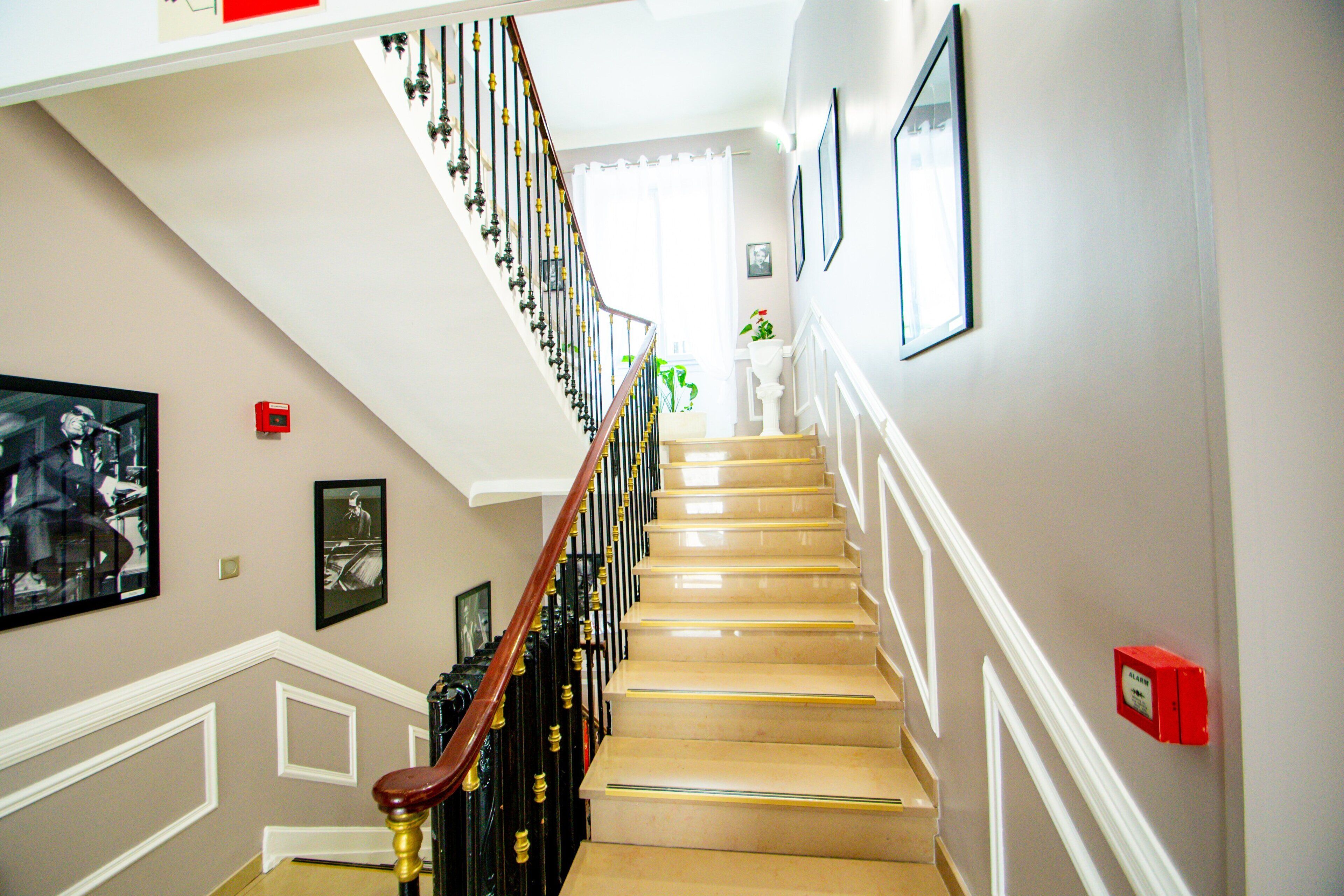 A staircase with a wooden handrail and black balusters, white trim, and a red fire alarm box on the wall.