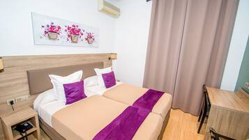 Een tweepersoonsbed met een houten hoofdbord, een nachtkastje met een telefoon, en een wandairconditioner.