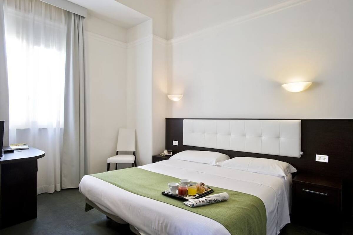 A hotel room with a bed, a desk, a chair, and a nightstand.