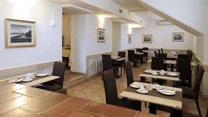 Un comedor con mesas y sillas, cuadros en las paredes y una escalera que sube a otro nivel.