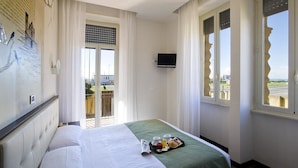 Habitación de hotel con cama, televisión, balcón con vistas y bandeja de desayuno sobre la cama.
