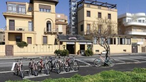Un hotel con un cartel llamativo que dice 'HOTEL', un área de estacionamiento con bicicletas y un cielo despejado.