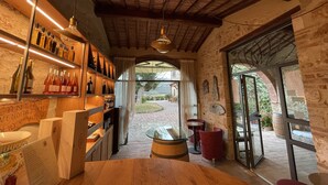 A rustic interior with wooden shelves displaying wine bottles, a glass table, and red chairs. - Il Colombaio Winery and Rooms (Monteriggioni)