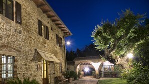 A stone building with a courtyard, potted plants, and a bench. - Il Colombaio Winery and Rooms (Monteriggioni)