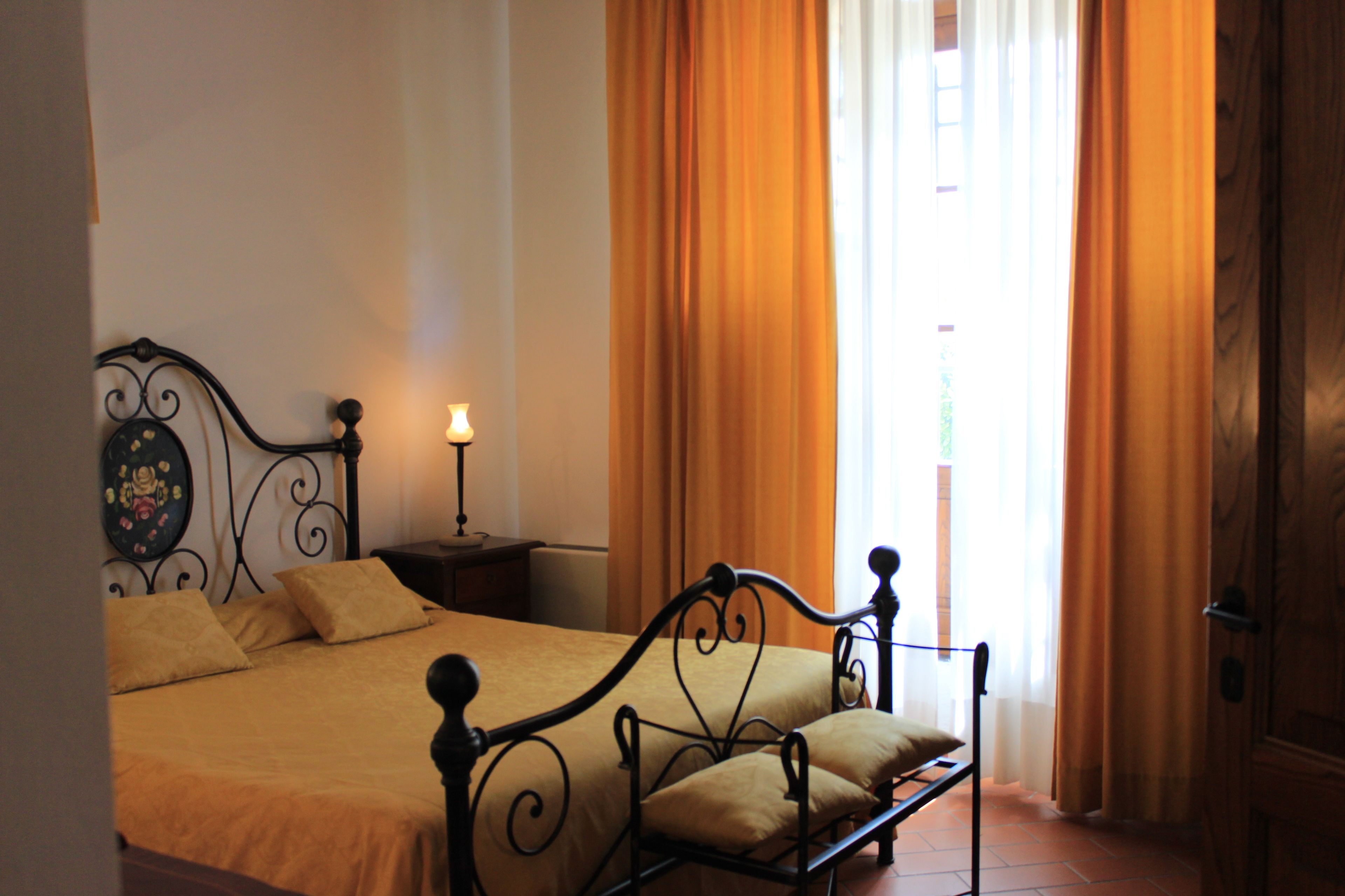 A neatly made bed with a headboard, a bedside table with a lamp, and a window with curtains.