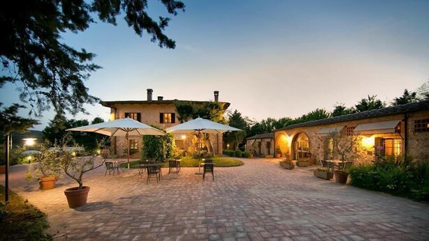 A courtyard with stone paving, outdoor seating, and a building with a rustic stone facade. - Il Colombaio Winery and Rooms (Monteriggioni)