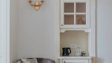 A room with a grey upholstered armchair, a white cabinet with a glass door, and a wall-mounted light fixture.