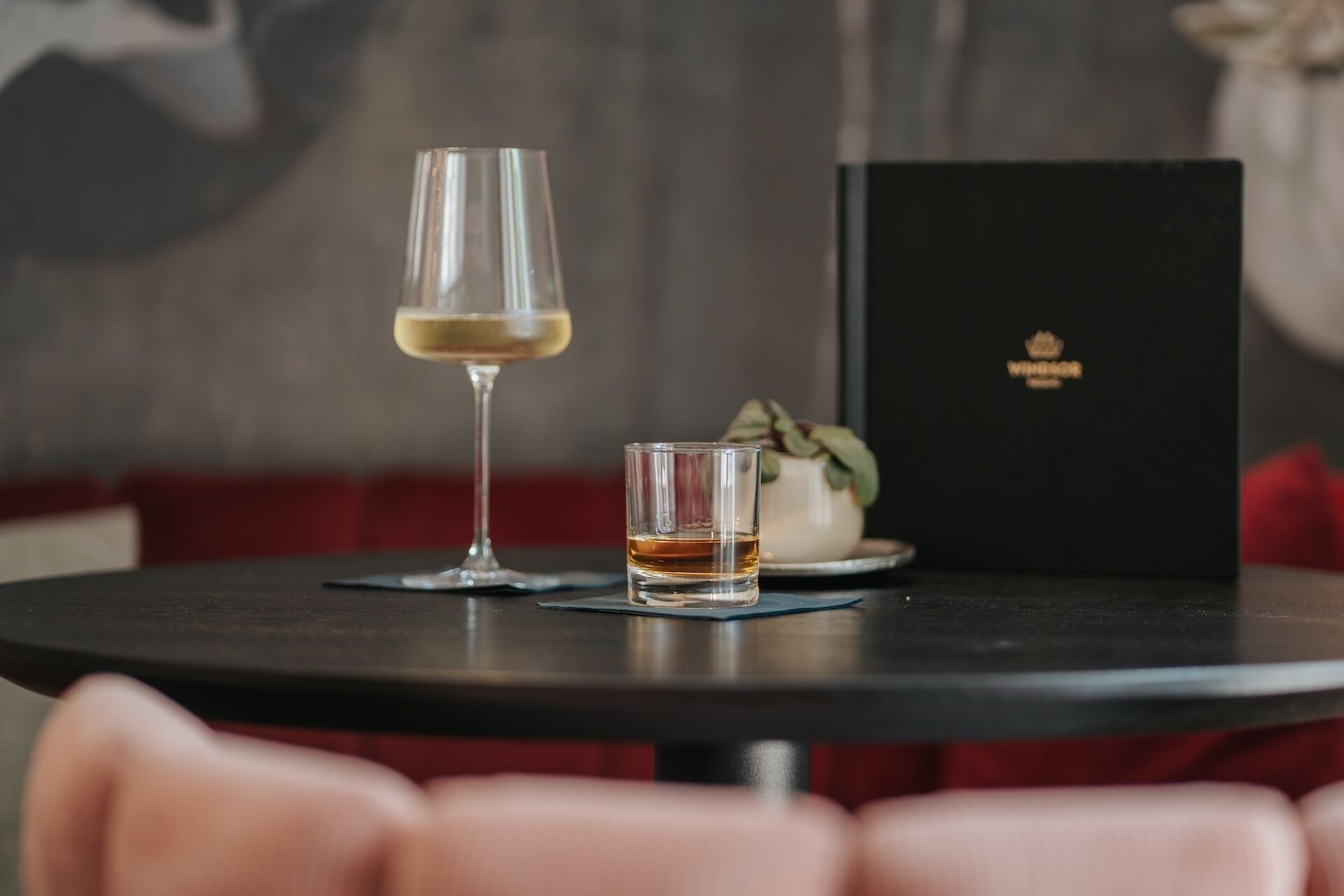A table with a wine glass and a shot glass, a small potted plant, and a black box with a logo.