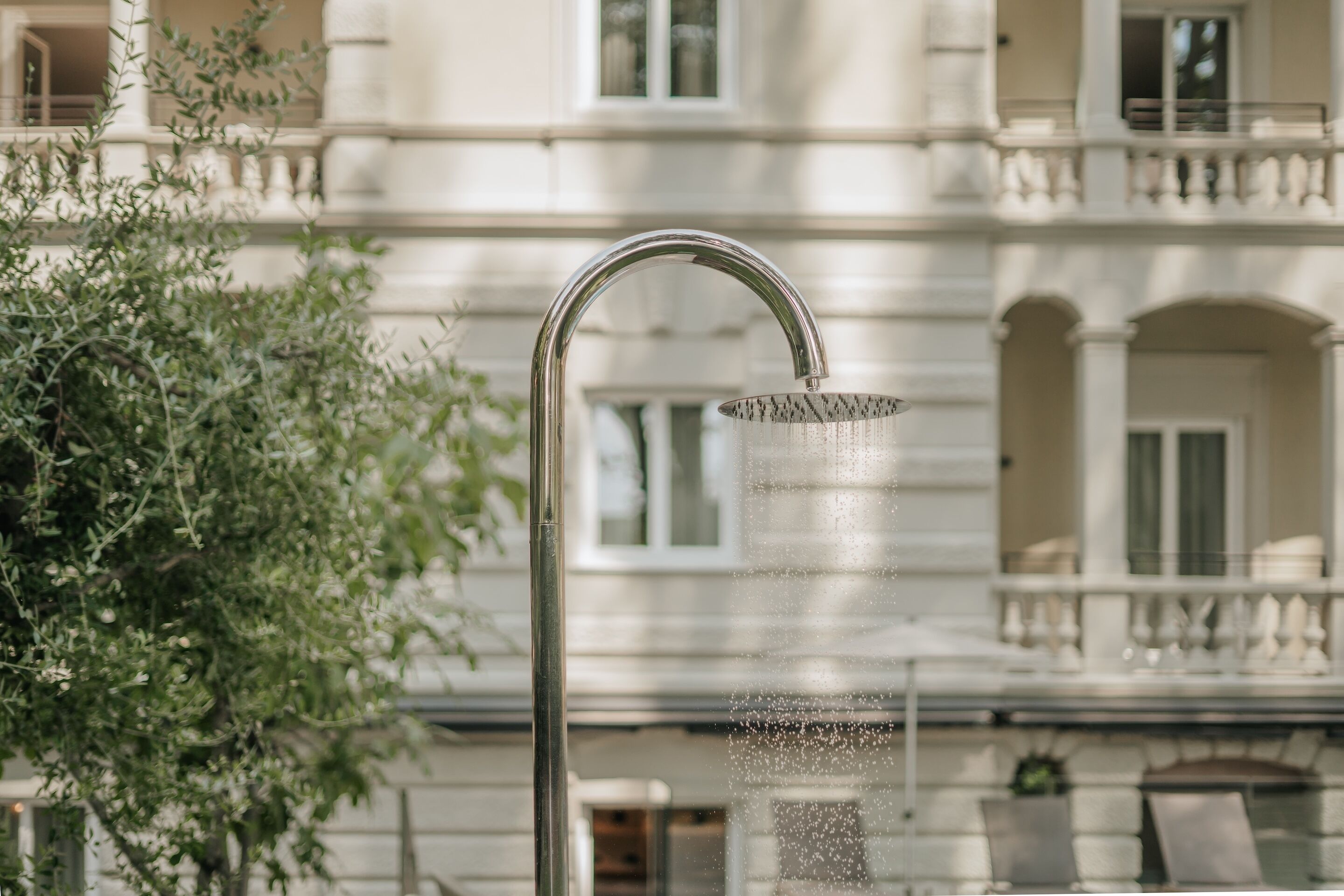 A modern outdoor shower with a curved spout, set against a building with balconies and windows.