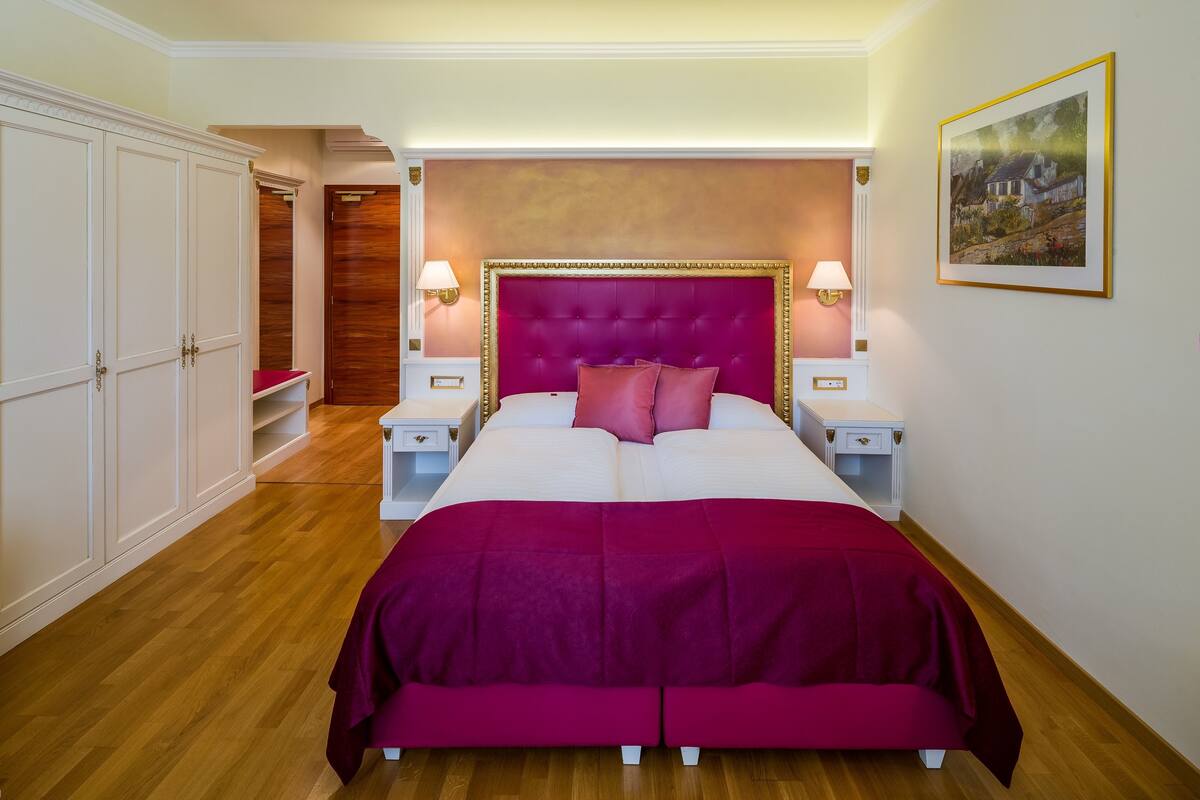 A bedroom with a large bed, two bedside tables, a wardrobe, and a painting on the wall.