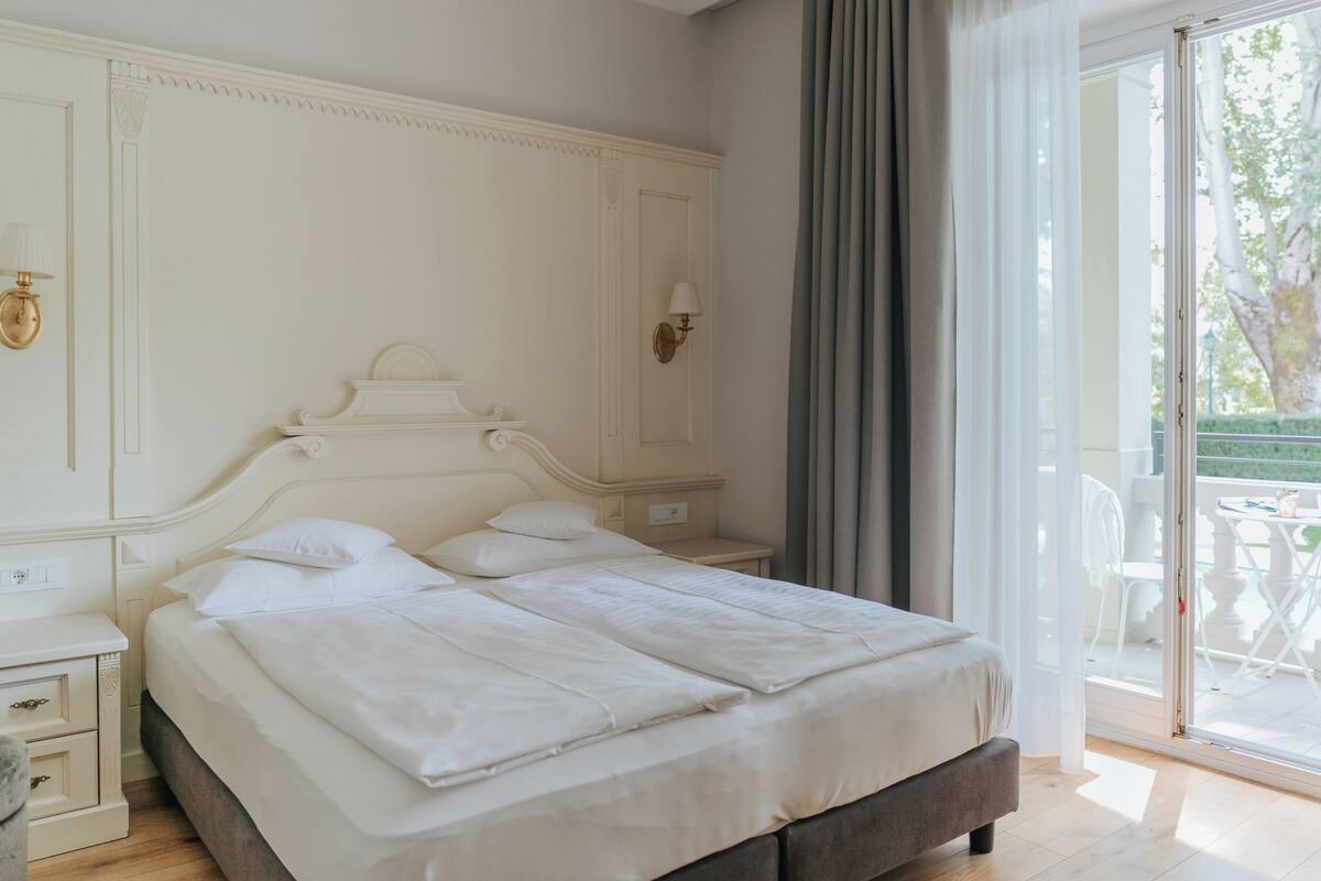 A bedroom with a large bed, a nightstand, a wall-mounted lamp, and a sliding glass door leading to an outdoor area.