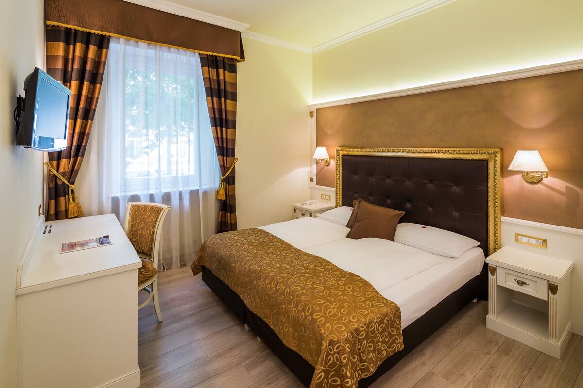 A hotel room with a large bed, a desk, a chair, a television, and two bedside lamps.