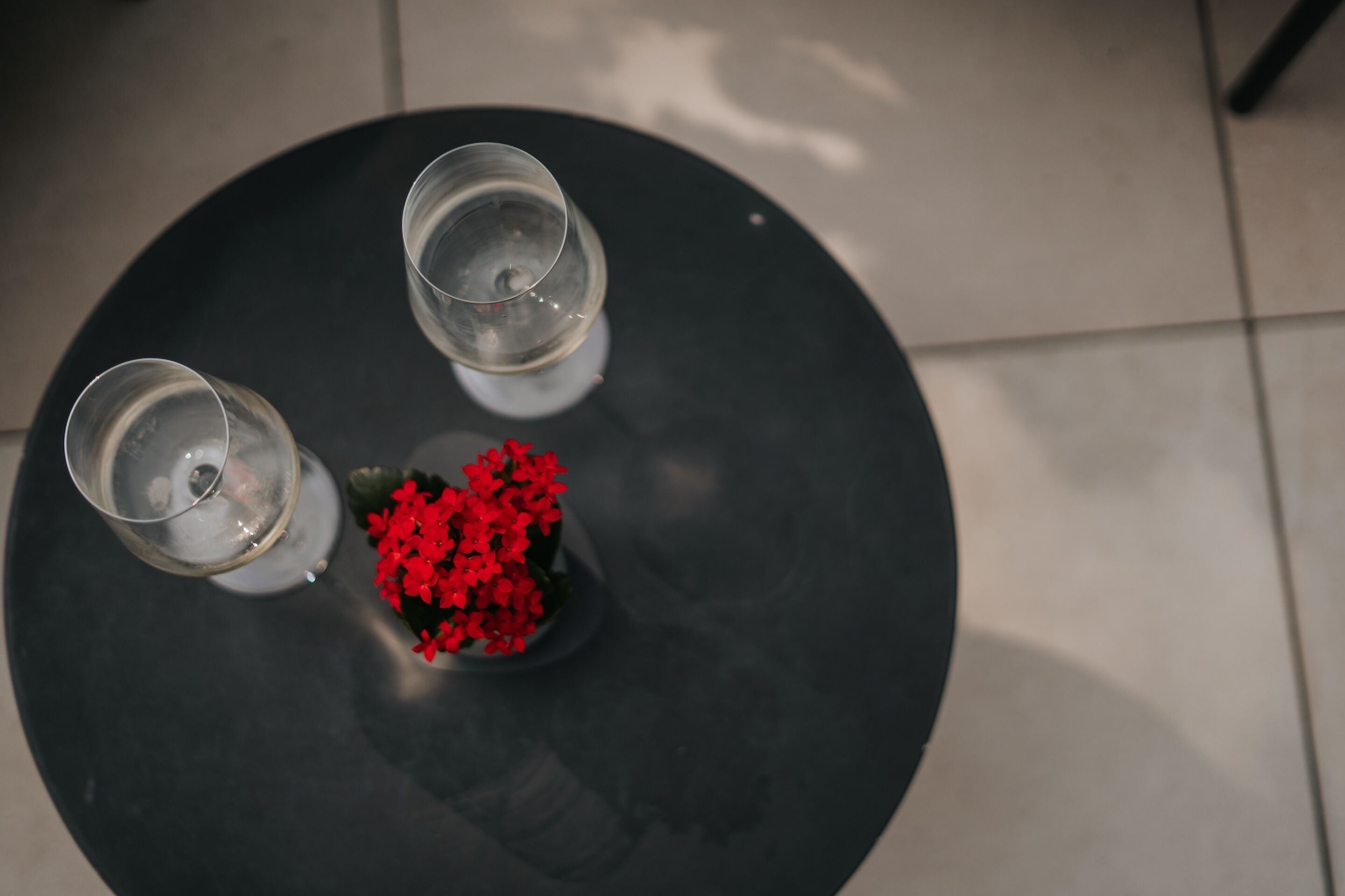 A round table with two glasses and a small red flower arrangement.