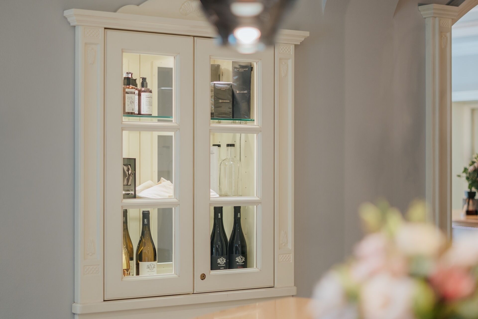 A white cabinet with glass doors containing various bottles and items.