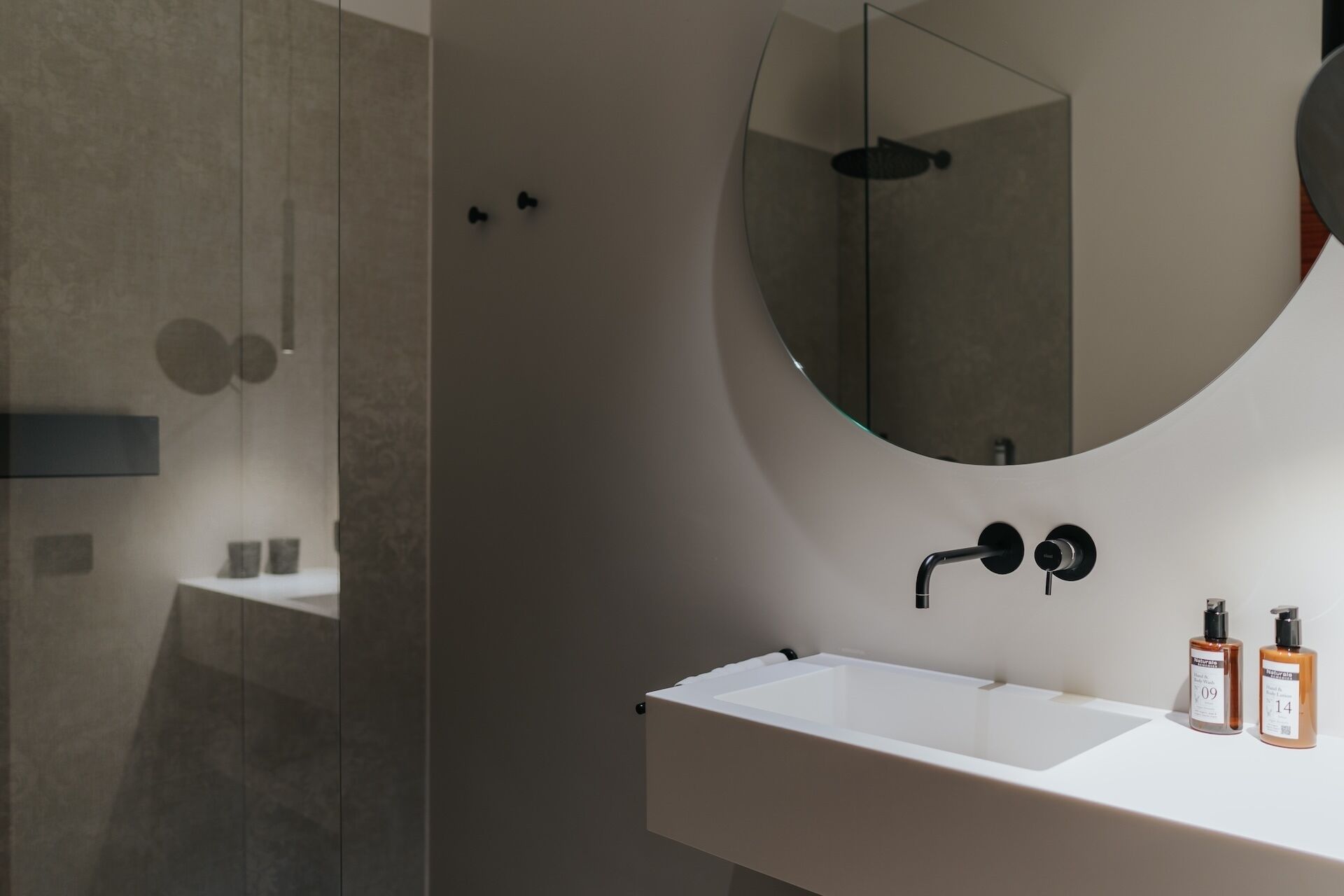 A modern bathroom with a large mirror, a sink, and two bottles of shampoo.