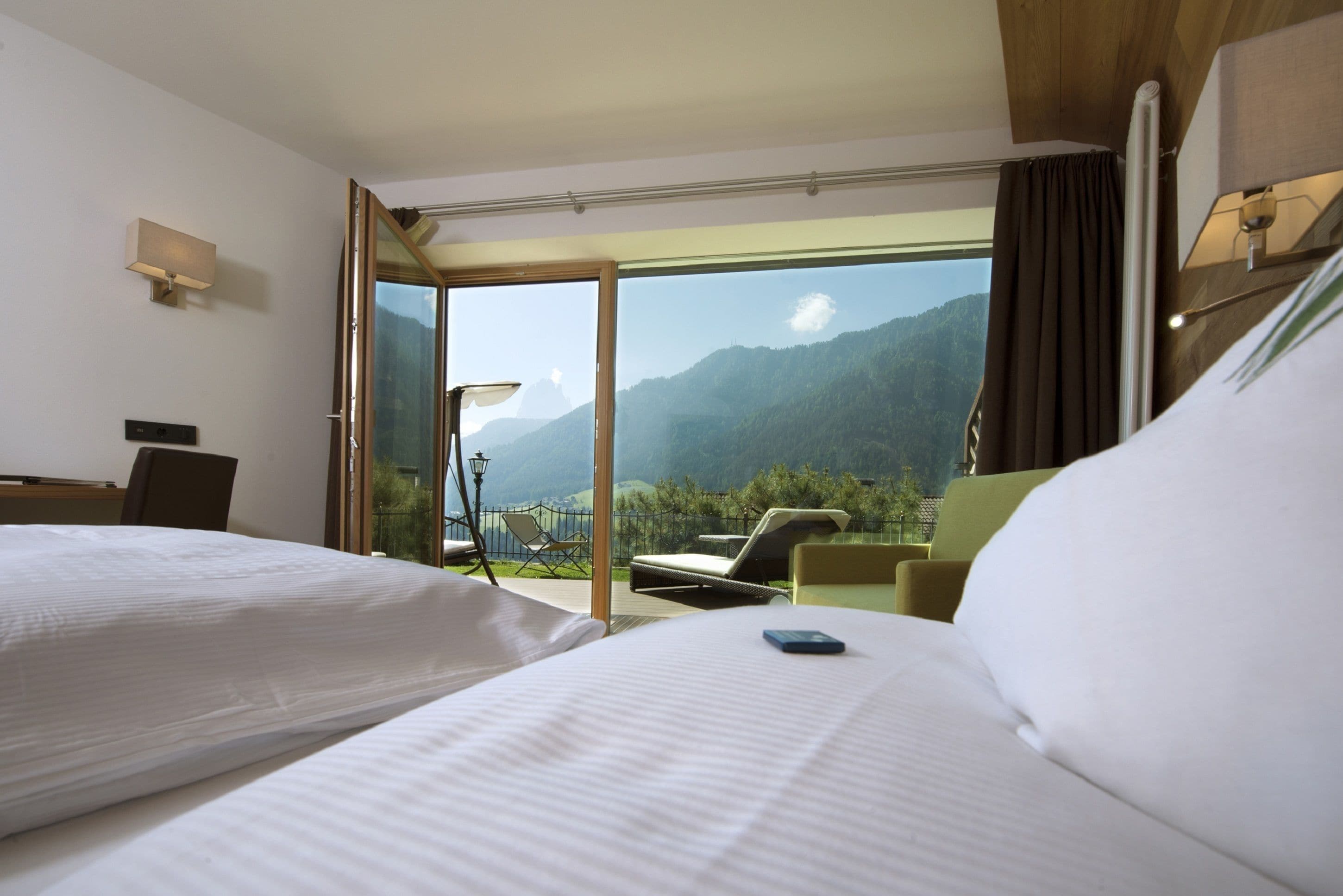 Habitación de hotel con dos camas, un balcón con una silla y vistas a las montañas.